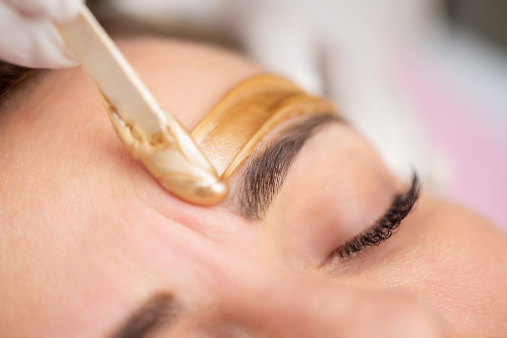 Applying Gold Colored Wax with Spatula on Woman's Face - stock photo